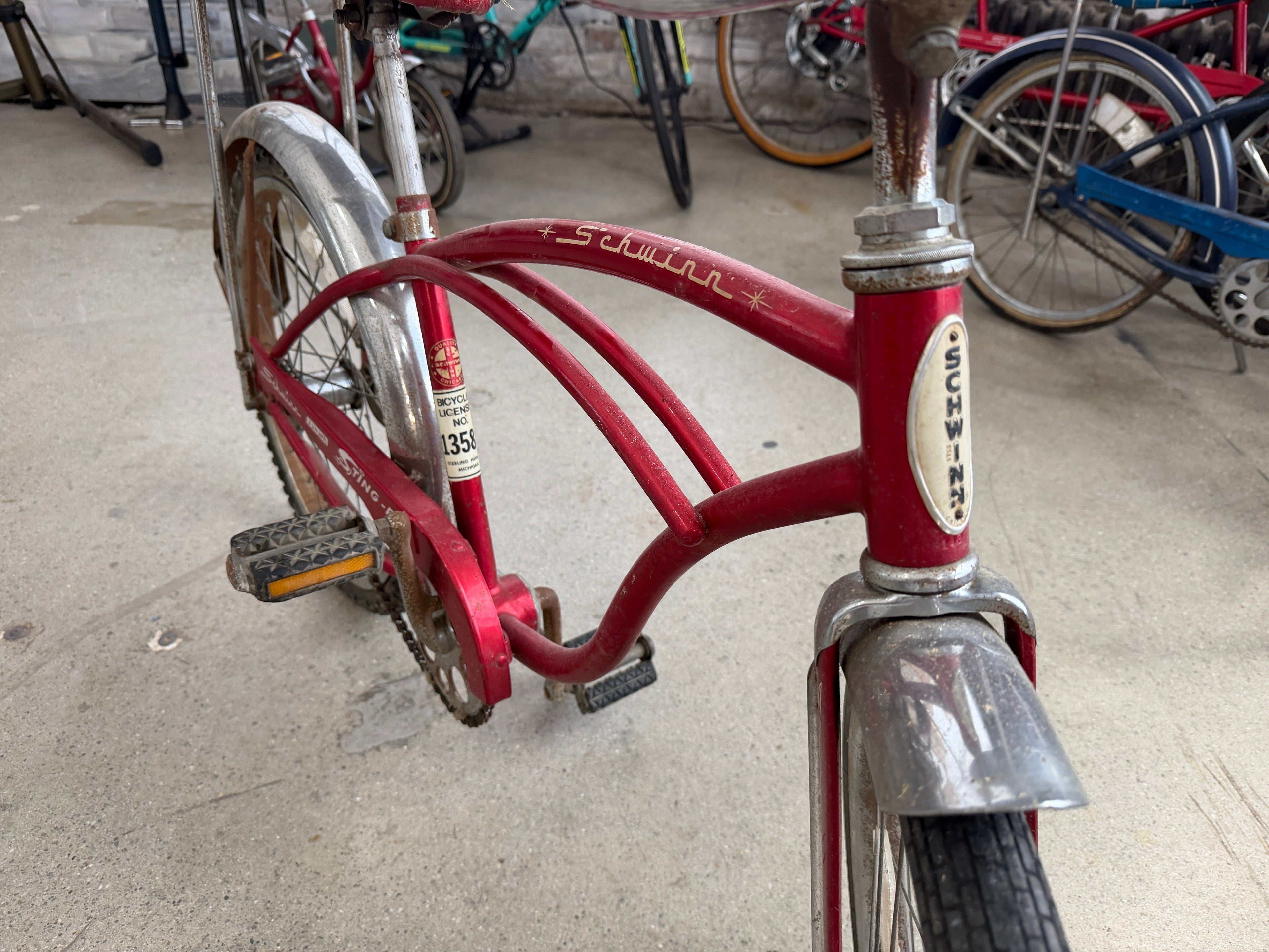Close-up of Schwinn Junior Sting-Ray frame showing original Schwinn head badge, red frame detail, chrome fork, and vintage Michigan bicycle license No. 1358 — The Foundry Pontiac