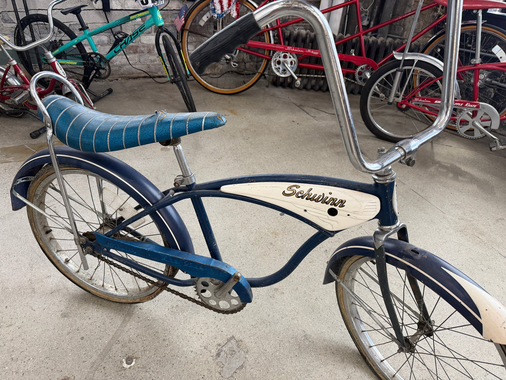Vintage Schwinn Typhoon bicycle in blue with white tank-style insert, banana seat, tall sissy bar, chrome fenders, and high-rise handlebars — full side profile at The Foundry by History Loves Company in downtown Pontiac, Michigan