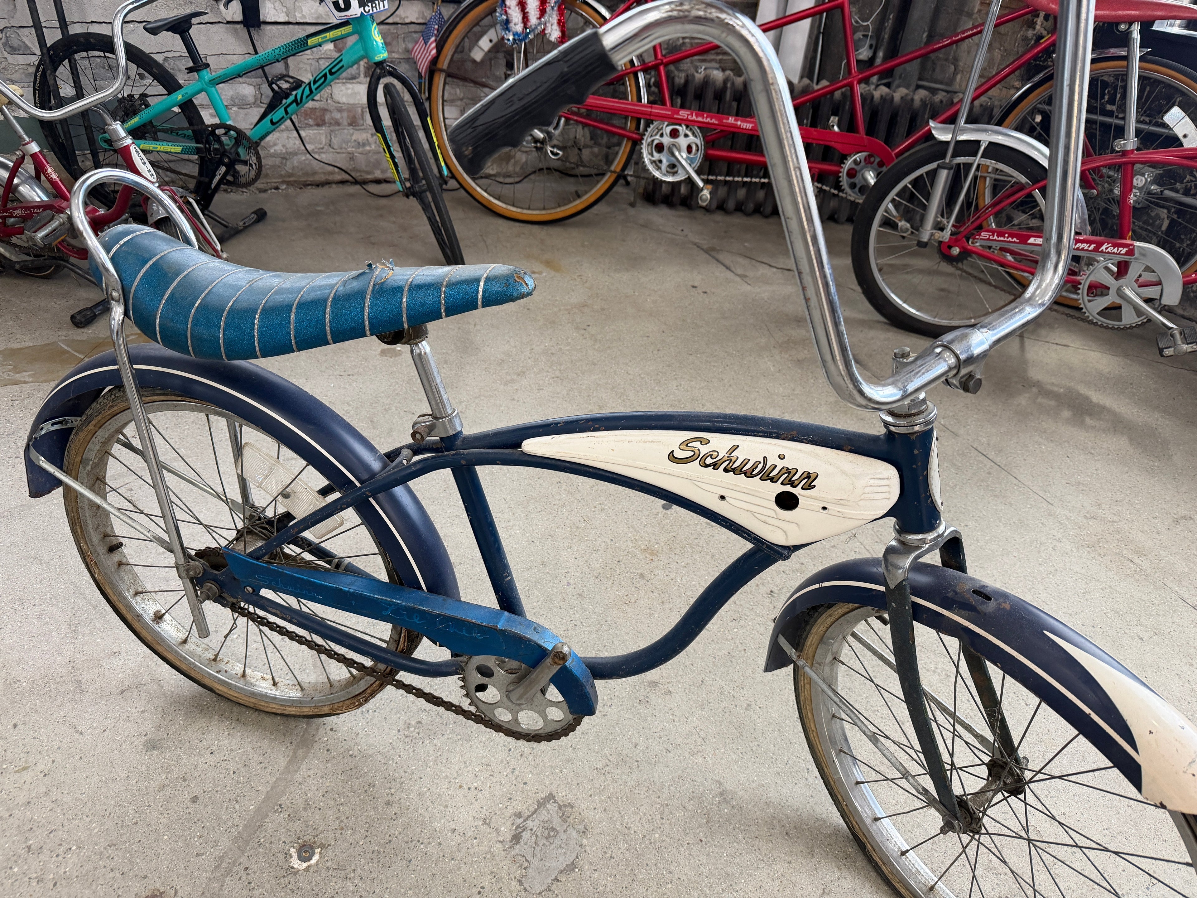 Vintage Schwinn Typhoon bicycle in blue with white tank-style insert, banana seat, tall sissy bar, chrome fenders, and high-rise handlebars — full side profile at The Foundry by History Loves Company in downtown Pontiac, Michigan