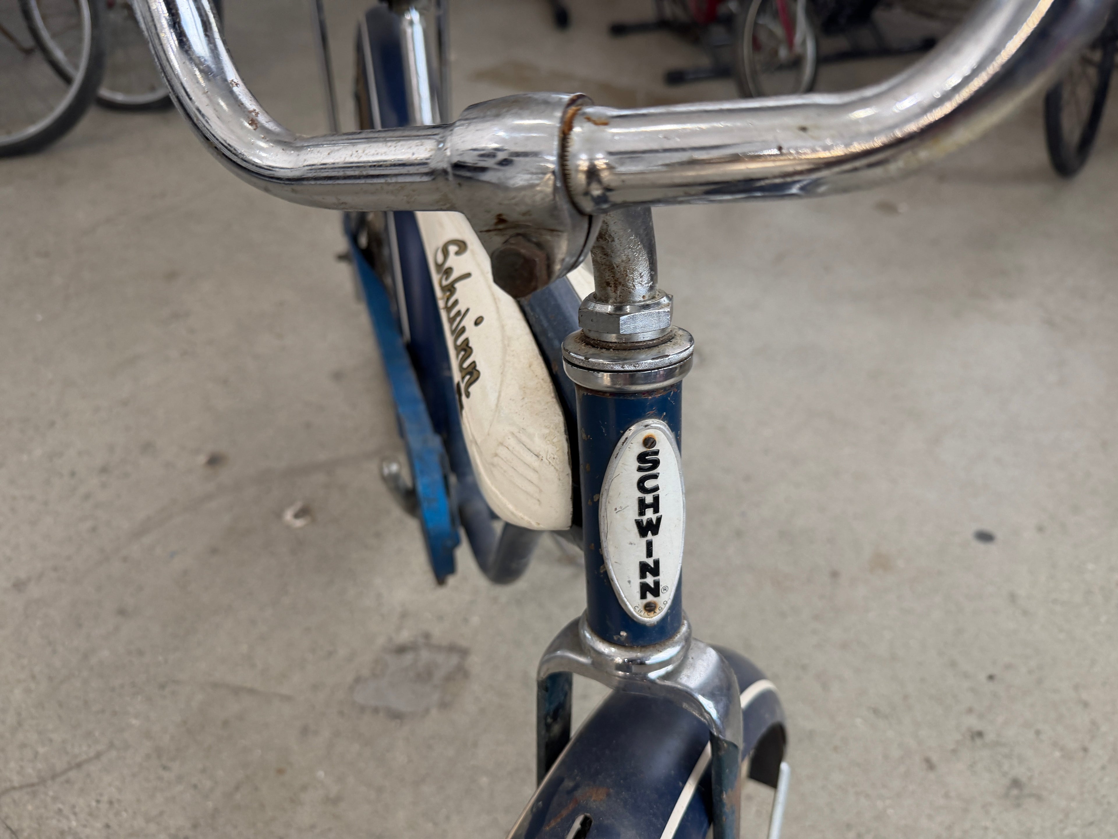Schwinn Typhoon original oval head badge on blue frame with chrome high-rise handlebars and Schwinn tank insert visible in background — The Foundry by History Loves Company