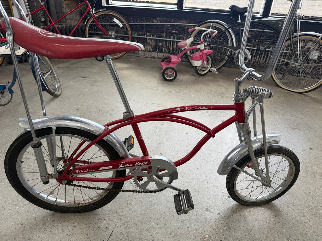 Vintage Schwinn Sting-Ray Apple Krate bicycle in red with banana seat, tall sissy bar, chrome fenders, springer-style front fork, and high-rise handlebars — full side profile at The Foundry by History Loves Company in downtown Pontiac, Michigan