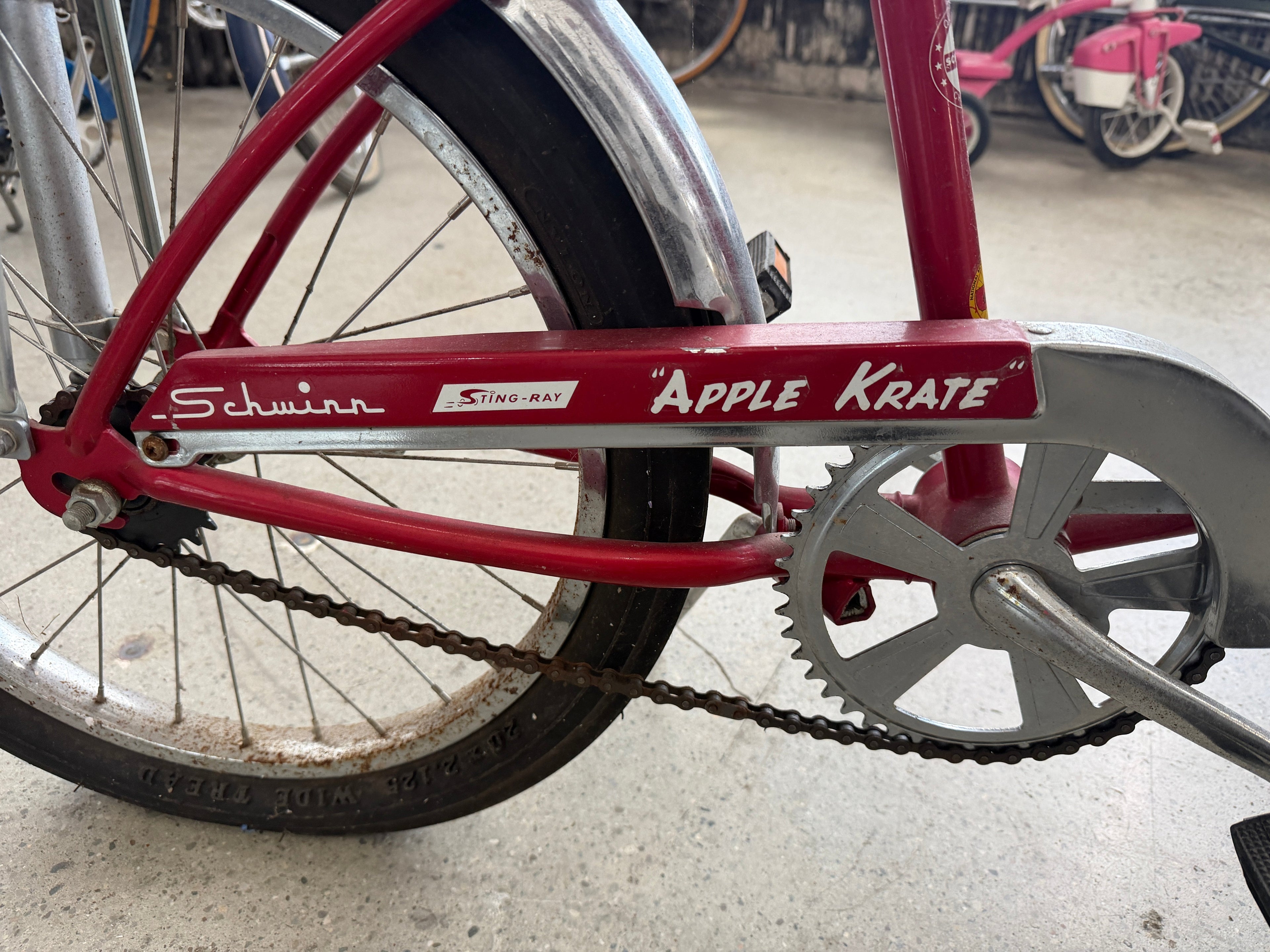 Close-up of Schwinn Sting-Ray Apple Krate chain guard showing original Apple Krate and Sting-Ray graphics on red frame with chrome sprocket — vintage muscle bike at The Foundry Pontiac