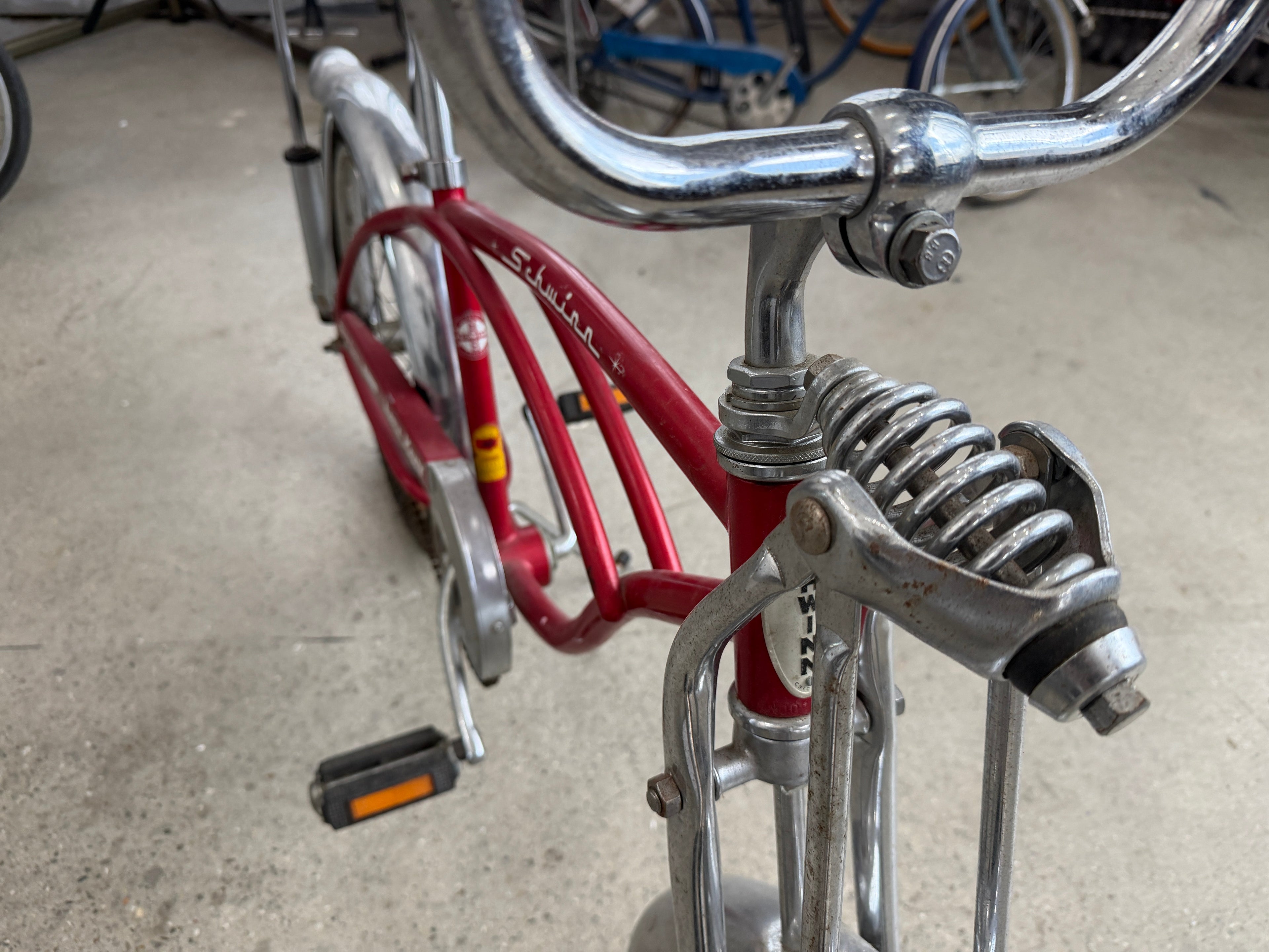 Schwinn Apple Krate springer-style front fork with chrome coil springs, high-rise handlebars, and Schwinn script on red frame — vintage Sting-Ray muscle bike detail at The Foundry by History Loves Company