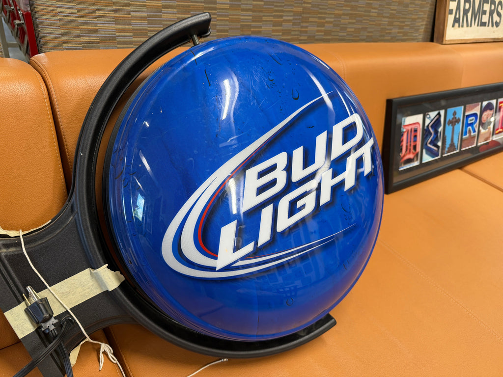 Bud Light double-sided illuminated bar sign showing classic blue Bud Light logo side with black hanging-style round frame and power cord — bar sign on consignment at The Foundry Pontiac