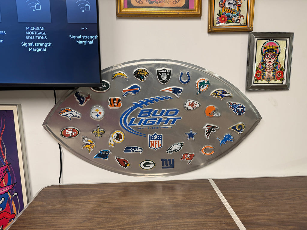 Bud Light NFL Official Beer Sponsor football-shaped wall sign with brushed-metal background and all 32 NFL team logos surrounding the Bud Light logo — full display view at The Foundry by History Loves Company in downtown Pontiac, Michigan