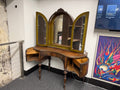 Antique tri-fold vanity dressing table with carved arched center mirror, folding side mirror doors, curved top surface, turned wood legs, side storage cabinets, and warm aged wood finish — on consignment at The Foundry by History Loves Company in downtown Pontiac, Michigan