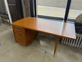 Mid-century modern wood executive desk with broad walnut-toned work surface, three-drawer left pedestal, brass-tone drawer pulls, tapered legs with brass-capped feet — vintage office furniture on consignment at The Foundry by History Loves Company in downtown Pontiac, Michigan