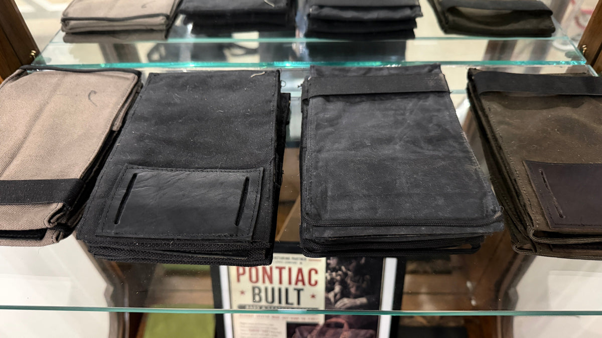 The Forge Hip Pack in all black woven canvas, Pontiac Built by The Foundry, stacked on glass shelf with Pontiac Built sign