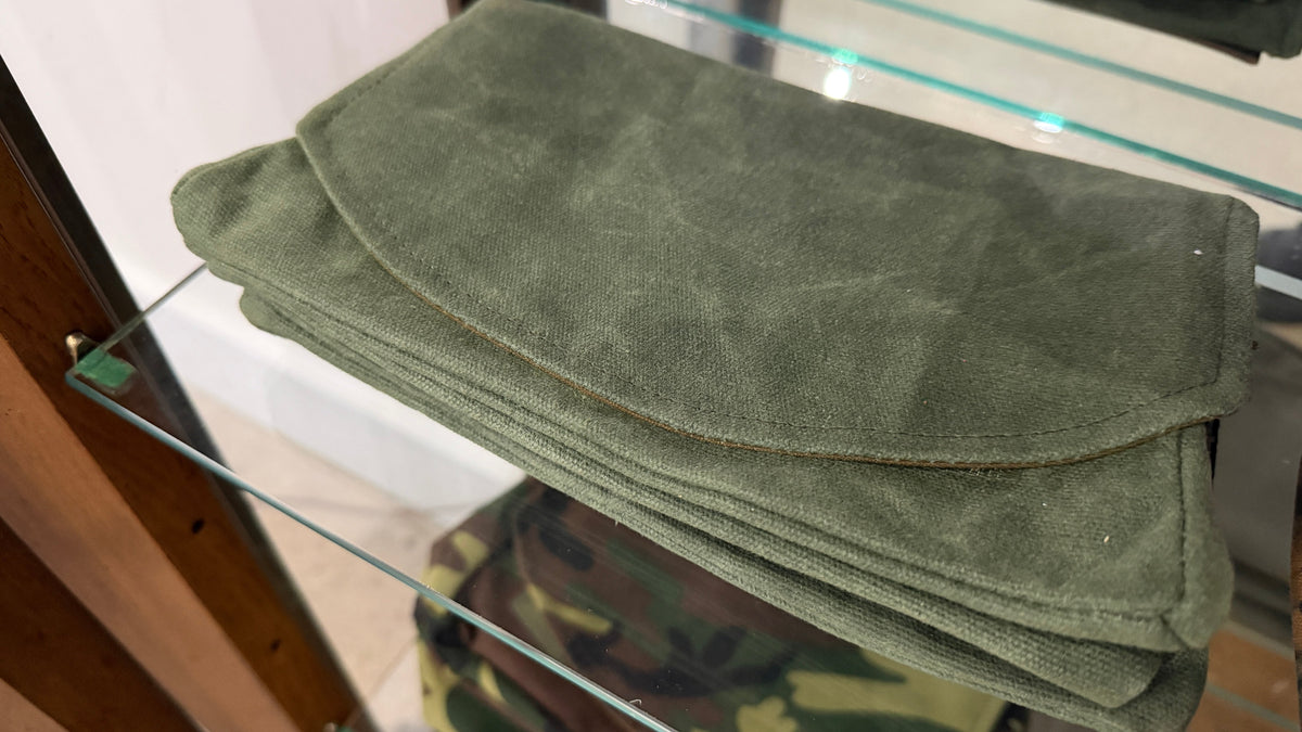 The Market Pouch in olive waxed canvas, stack of five, Pontiac Built by The Foundry on glass shelf