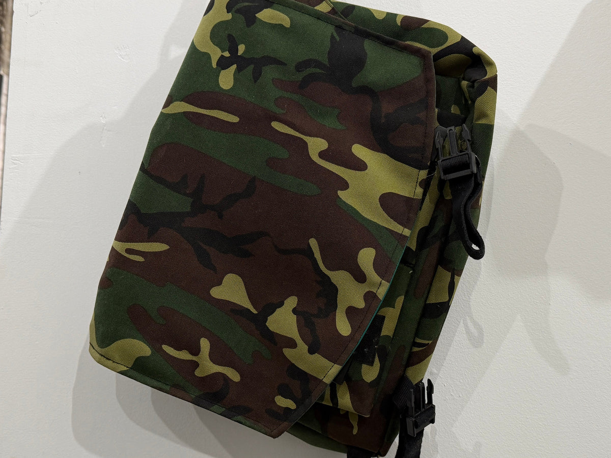 The Crosstown Sling Bag in woodland camo canvas with black buckle hardware and adjustable webbing strap, Pontiac Built by The Foundry