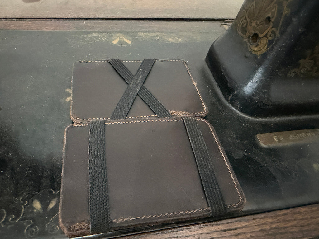 The Switch Wallet elastic band style — dark chocolate leather with black elastic X-cross and horizontal band, two wallets stacked, Pontiac Built