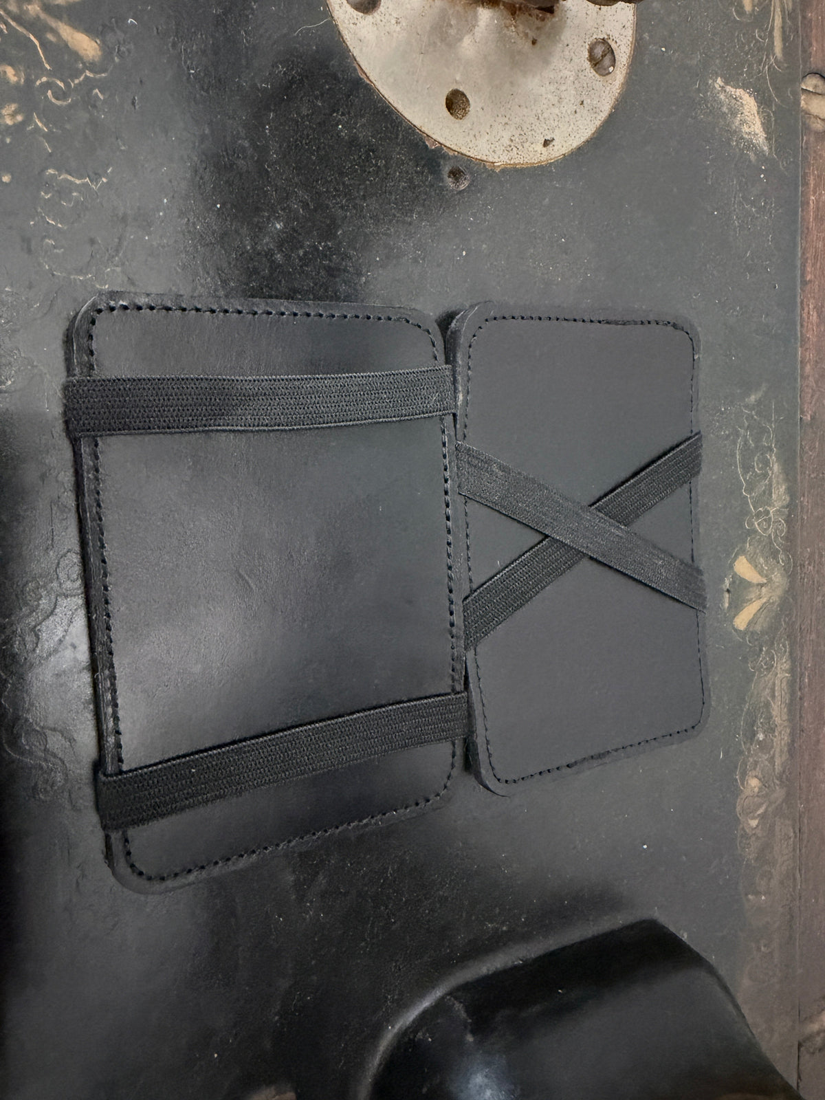 The Switch Wallet elastic band style open view — all black leather with black elastic X-cross on right panel and horizontal band on left, Pontiac Built