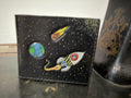 The Tradesman Wallet space scene back panel — hand-painted rocket ship, Earth, meteor and star field on dark espresso leather, cream saddle stitch