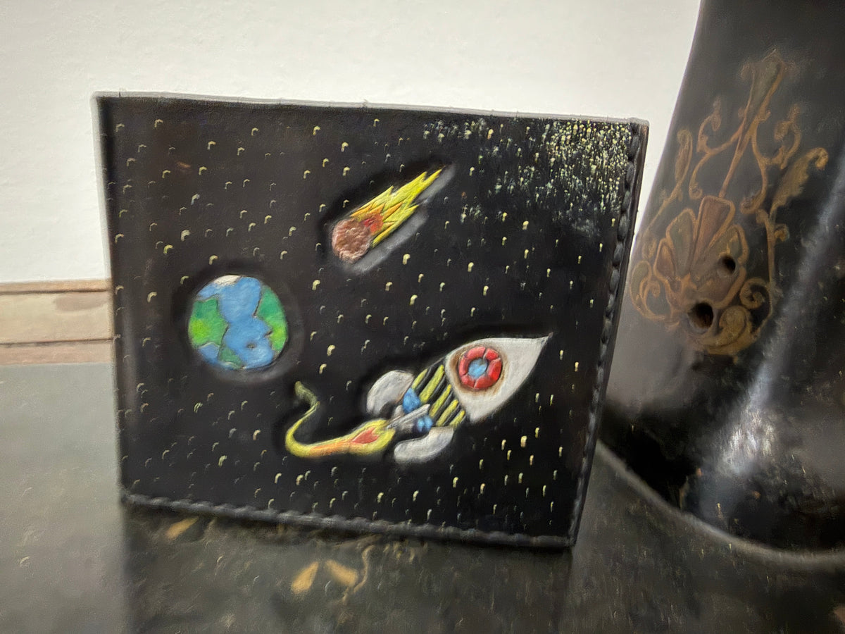 The Tradesman Wallet space scene back panel — hand-painted rocket ship, Earth, meteor and star field on dark espresso leather, cream saddle stitch