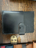 The Wayfarer Passport Wallet in jet black full-grain leather, snap closure tab, hand-stitched perimeter, open bifold view, Pontiac Built by The Foundry