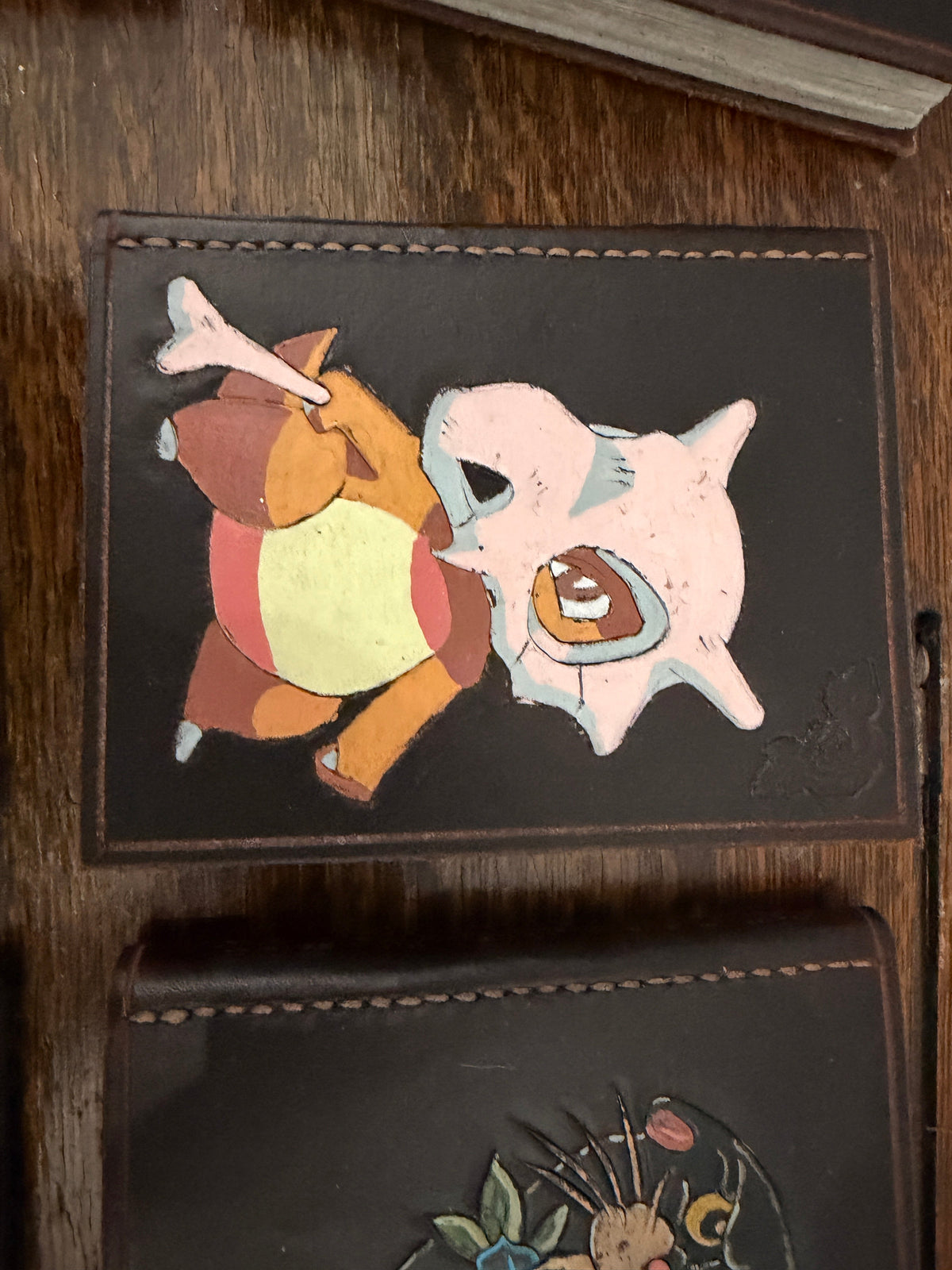 Handmade leather journal with hand-painted Cubone and Clefairy Pokemon design on dark leather cover, recycled card paper pages