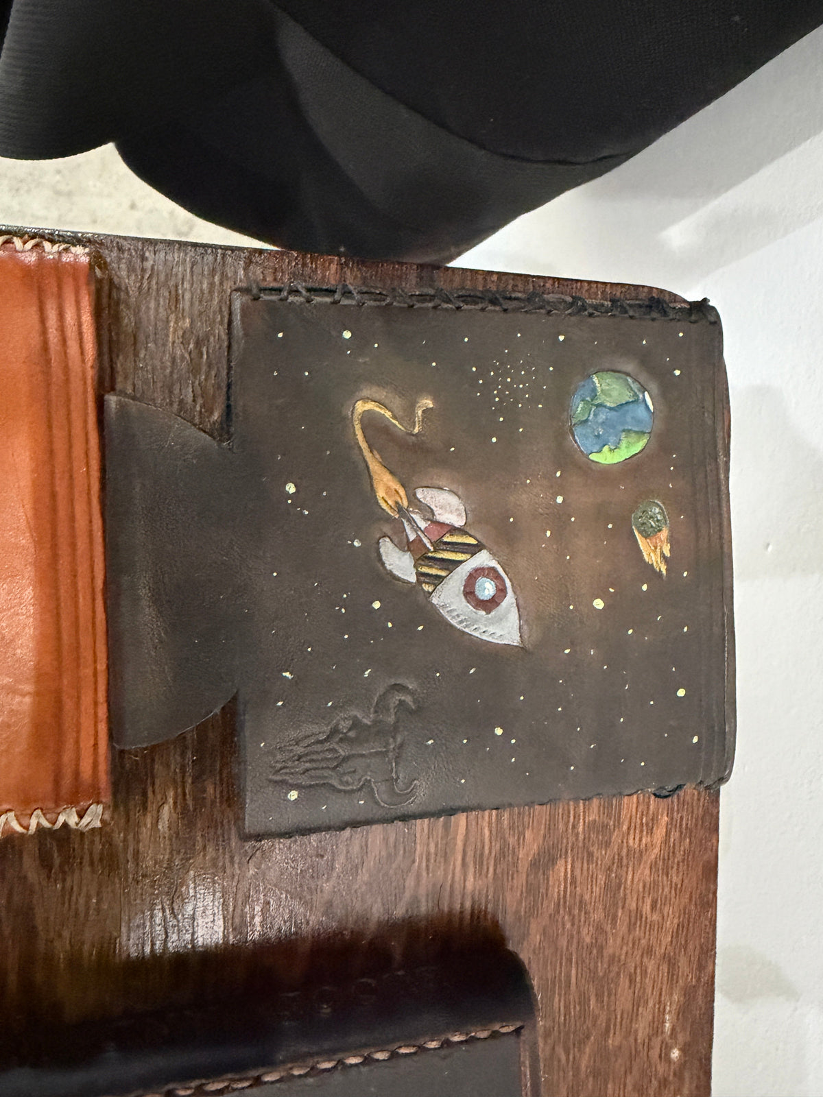 The Foundry Can Sleeve in dark espresso leather, hand-tooled and painted space scene — rocket ship, Earth, meteor, star field, Foundry maker mark