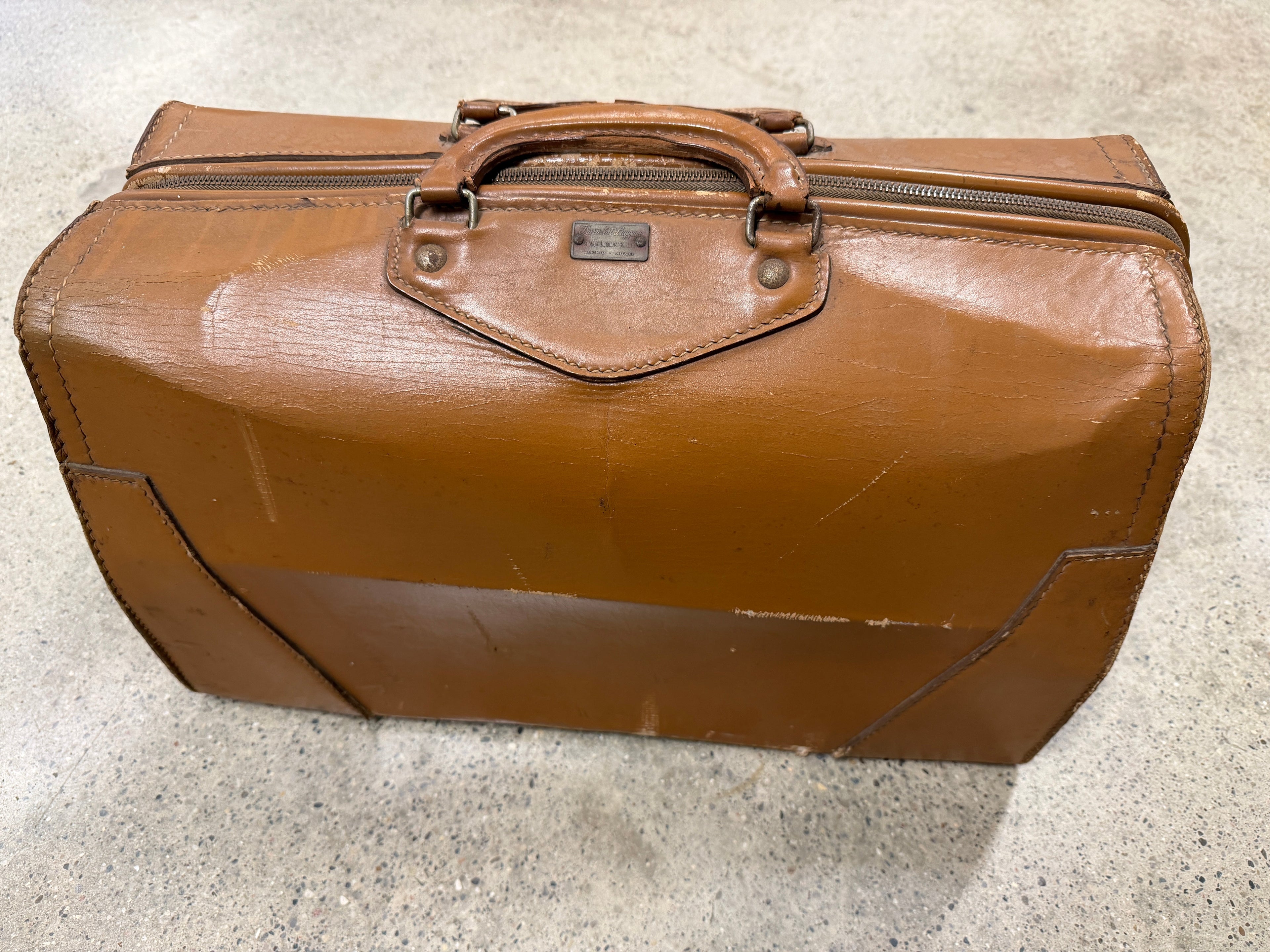 Vintage mid-century tan leather travel bag with full zip top, leather-wrapped handle, brass nameplate hardware, saddle-stitched panels, deep patina