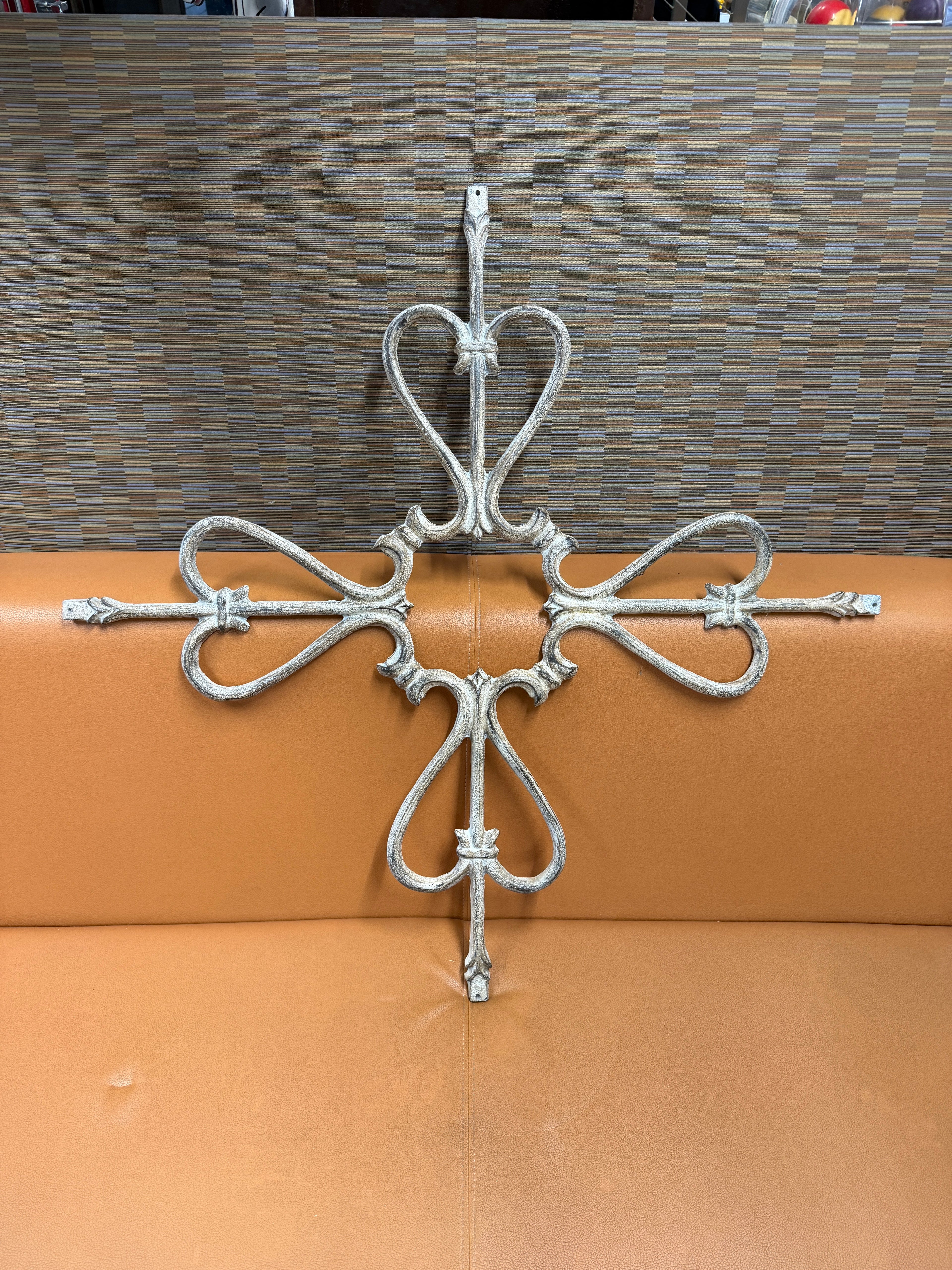 Vintage ornate iron architectural wall hanging in cross form with heart scroll loops, arrow arms, fleur-de-lis center, distressed white paint finish
