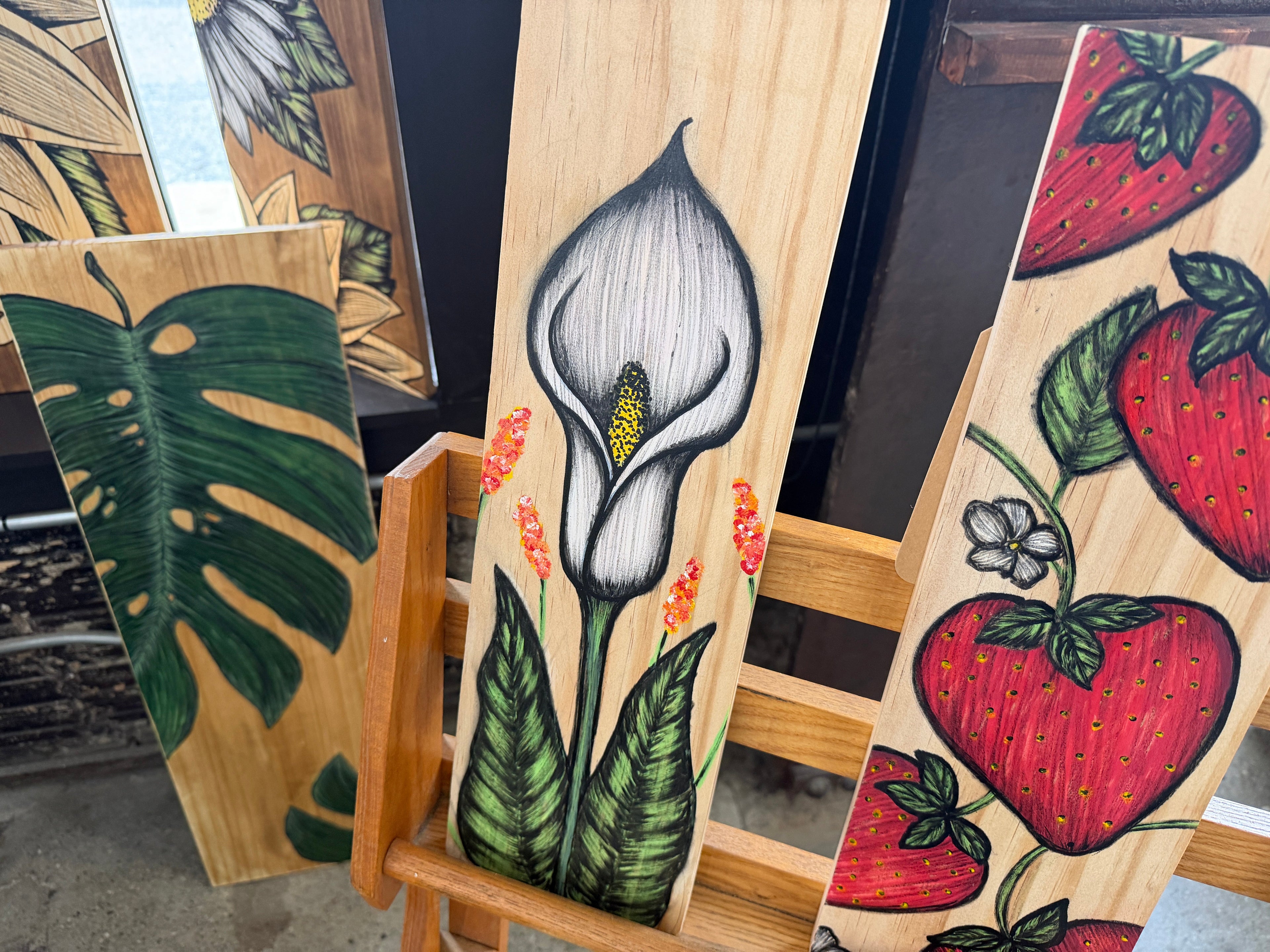Hand-drawn calla lily with green leaves and orange wildflowers on natural wood panel by Renee Reese